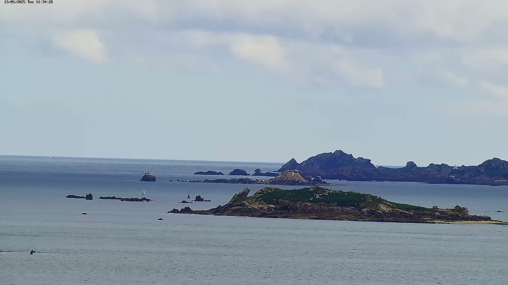 A calm, overcast day reveals a rocky island and several smaller islets surrounded by a vast expanse of sea.