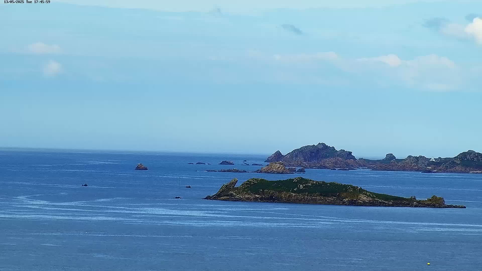 A mostly sunny day reveals a wide expanse of blue ocean dotted with small, rocky islands and a few distant boats.