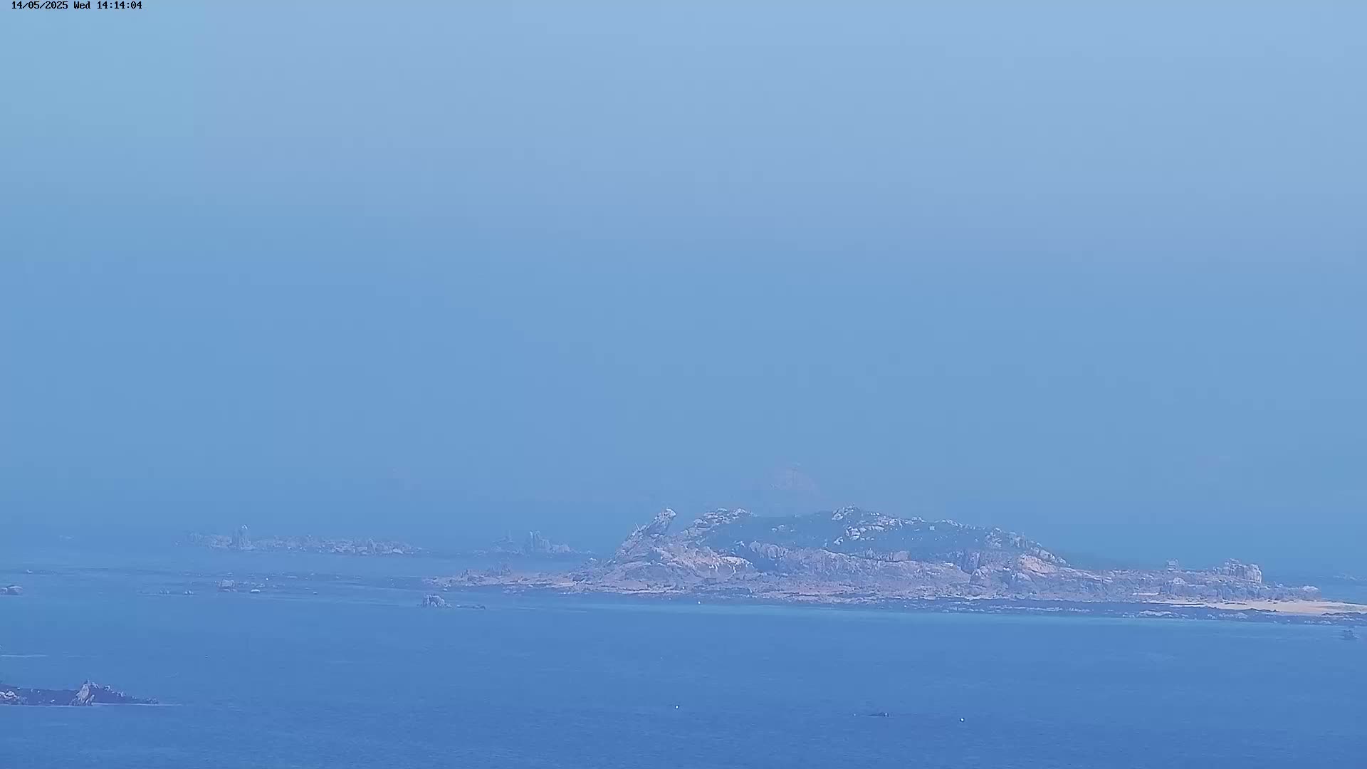 A hazy, distant view shows a rocky island surrounded by calm blue water and smaller rocky outcrops.