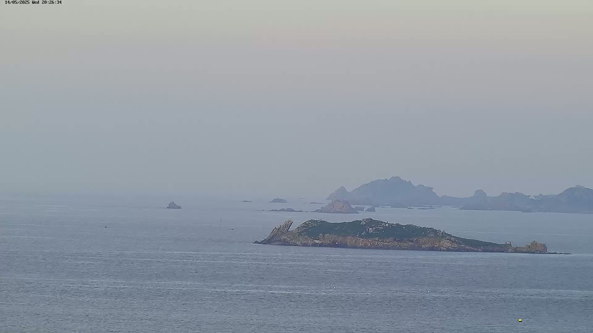 A hazy view of a small island with rocky terrain and sparse vegetation, surrounded by calm water and distant, indistinct landmasses.