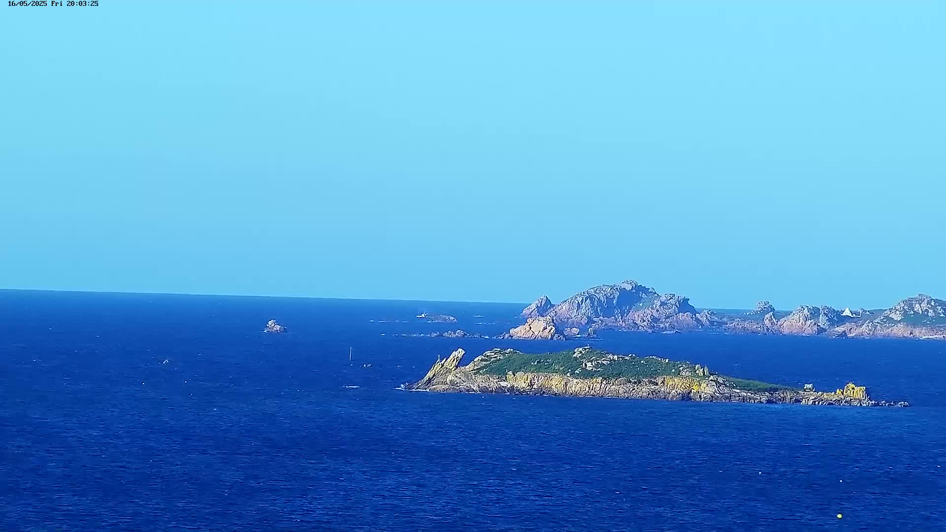 A calm, blue ocean stretches to the horizon under a clear blue sky, featuring several rocky islands and islets with sparse vegetation.