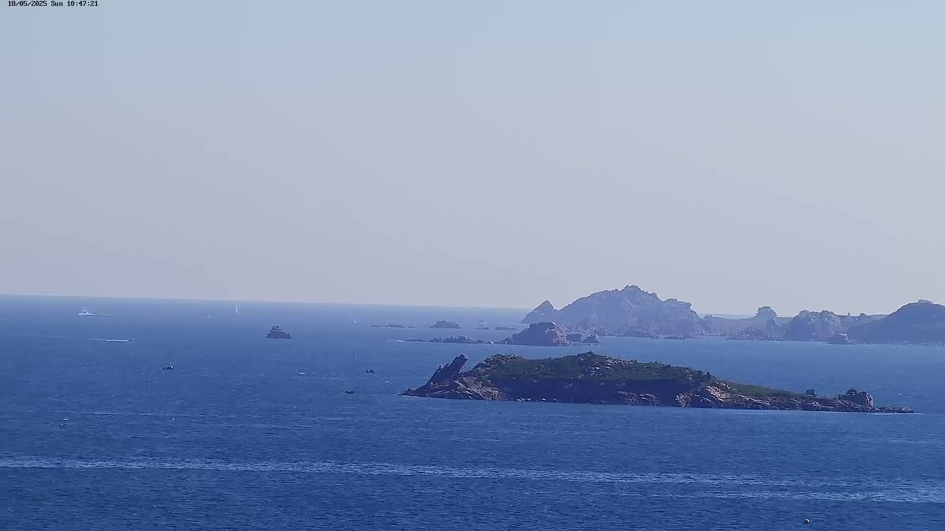 A hazy, sunny day reveals a calm expanse of blue ocean dotted with small boats and several rocky islands.
