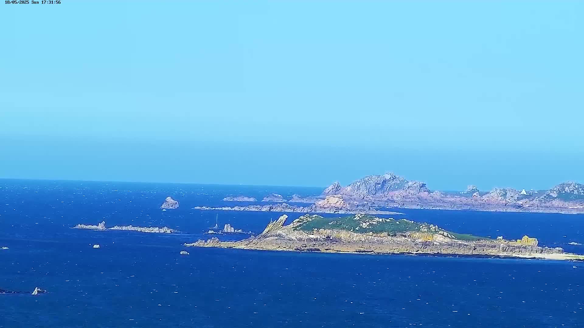 A clear, sunny day reveals a rocky island coastline and several smaller islands in a deep blue ocean.