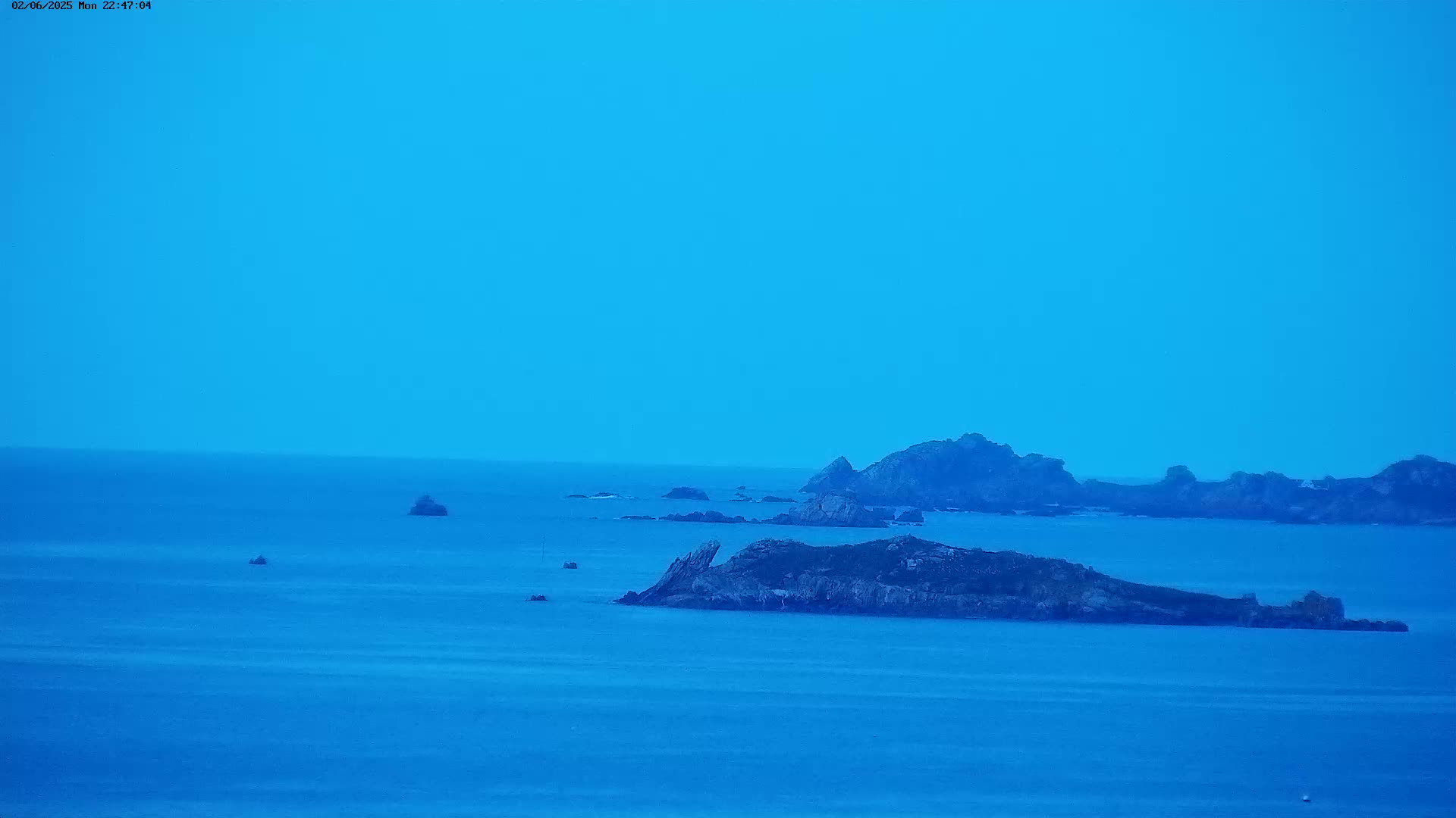 A dark blue sea stretches to the horizon under a clear, light blue sky, dotted with several rocky islands and small islets.