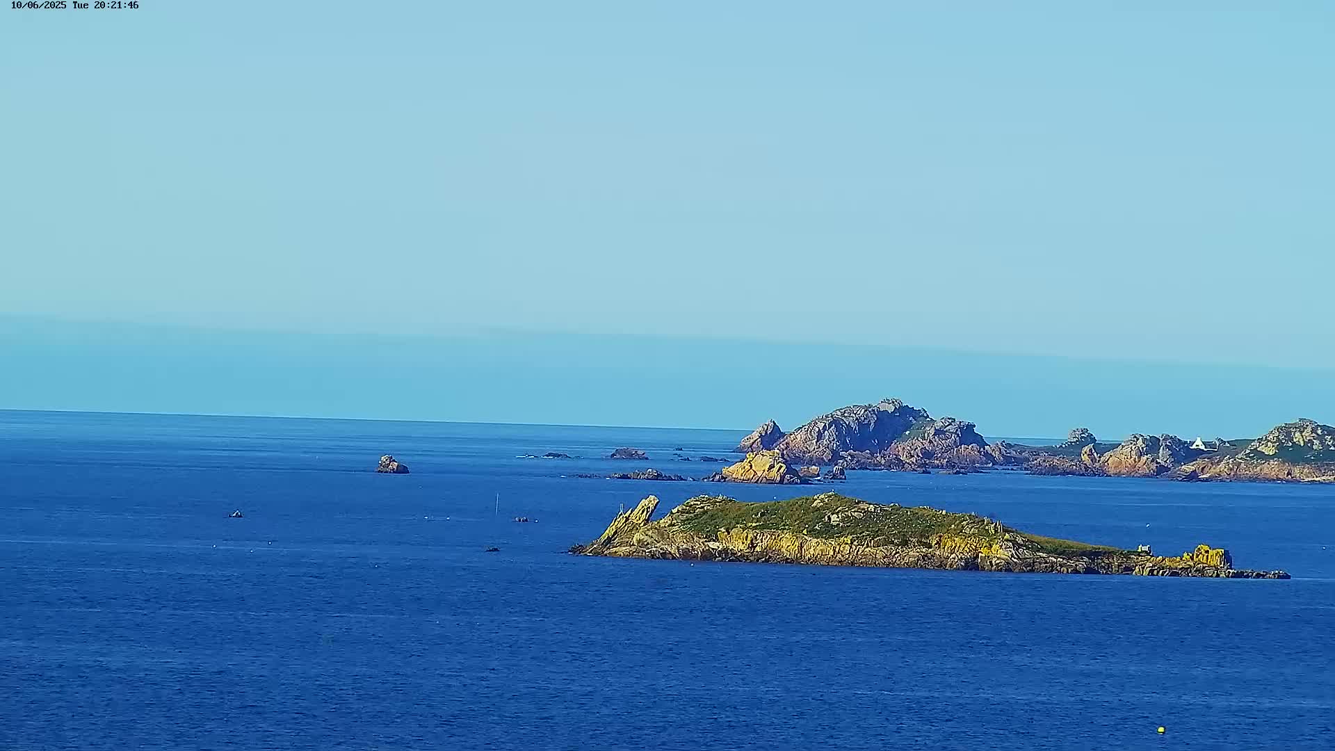 A tranquil ocean scene under a clear blue sky features several small rocky islands scattered across the water.