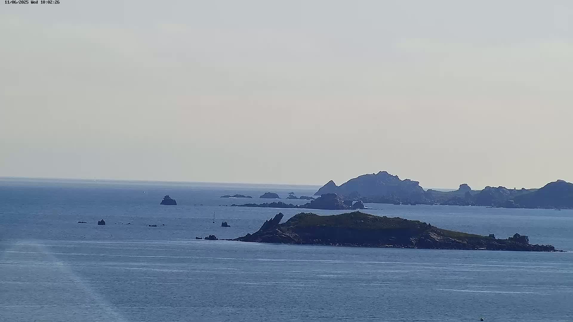 A tranquil ocean scene under a hazy sky shows several rocky islands and islets scattered across the water.
