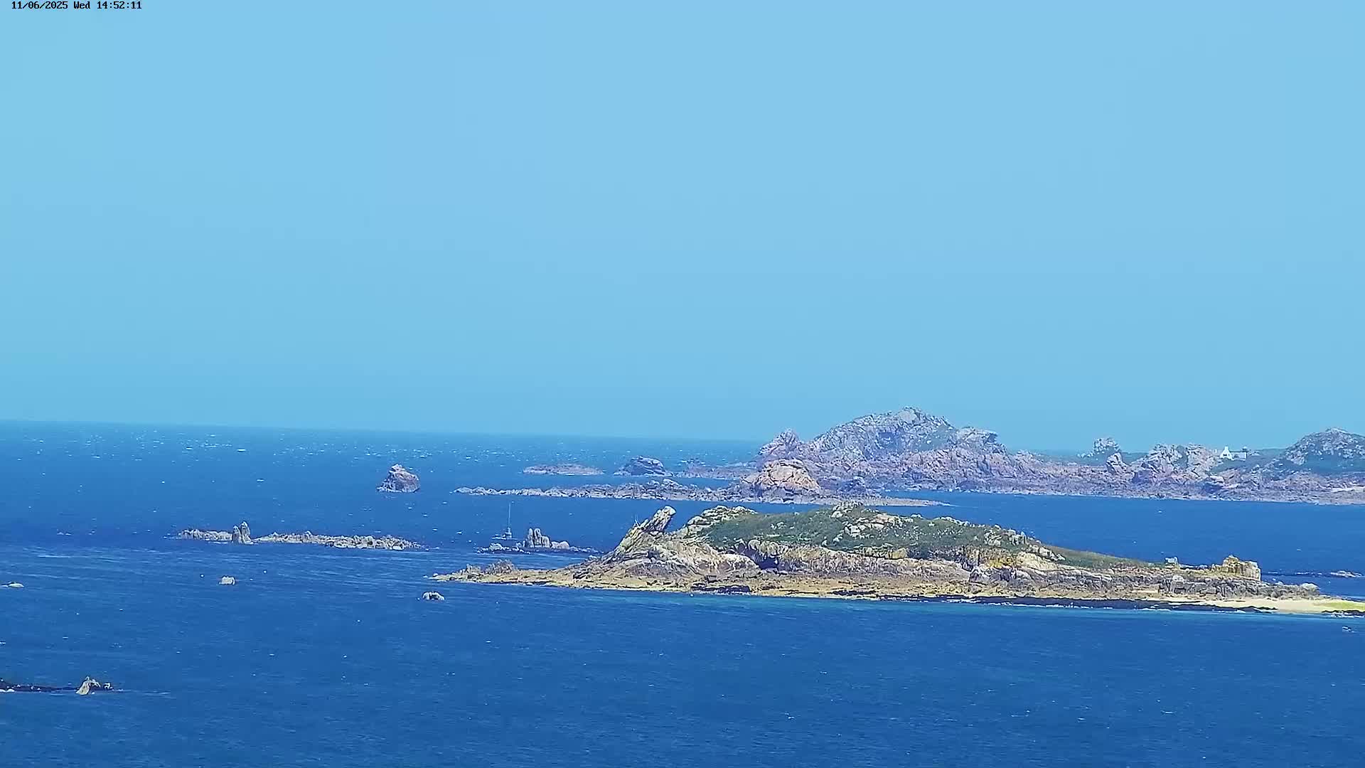 A sunny day reveals a tranquil ocean scene with several rocky islands and islets scattered across the water's surface.