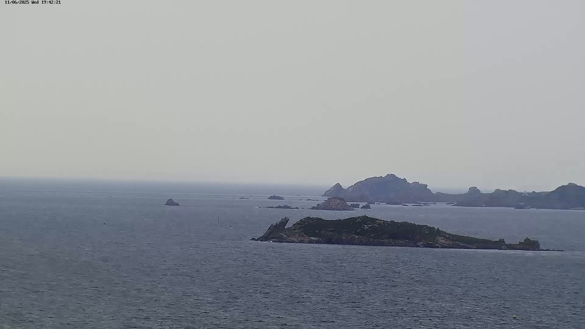 A hazy, overcast day reveals a vast expanse of ocean dotted with several rocky islands and outcroppings.