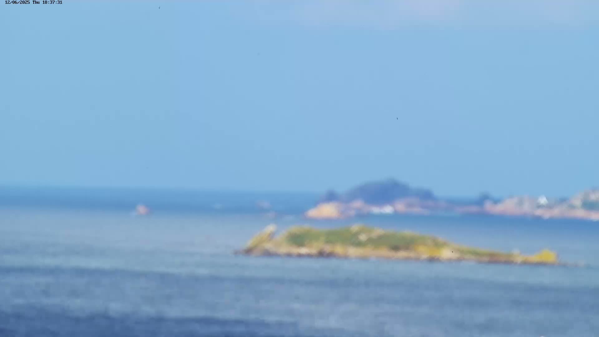 A small, vegetated island is visible in the distance across a calm, blue ocean under a clear sky.