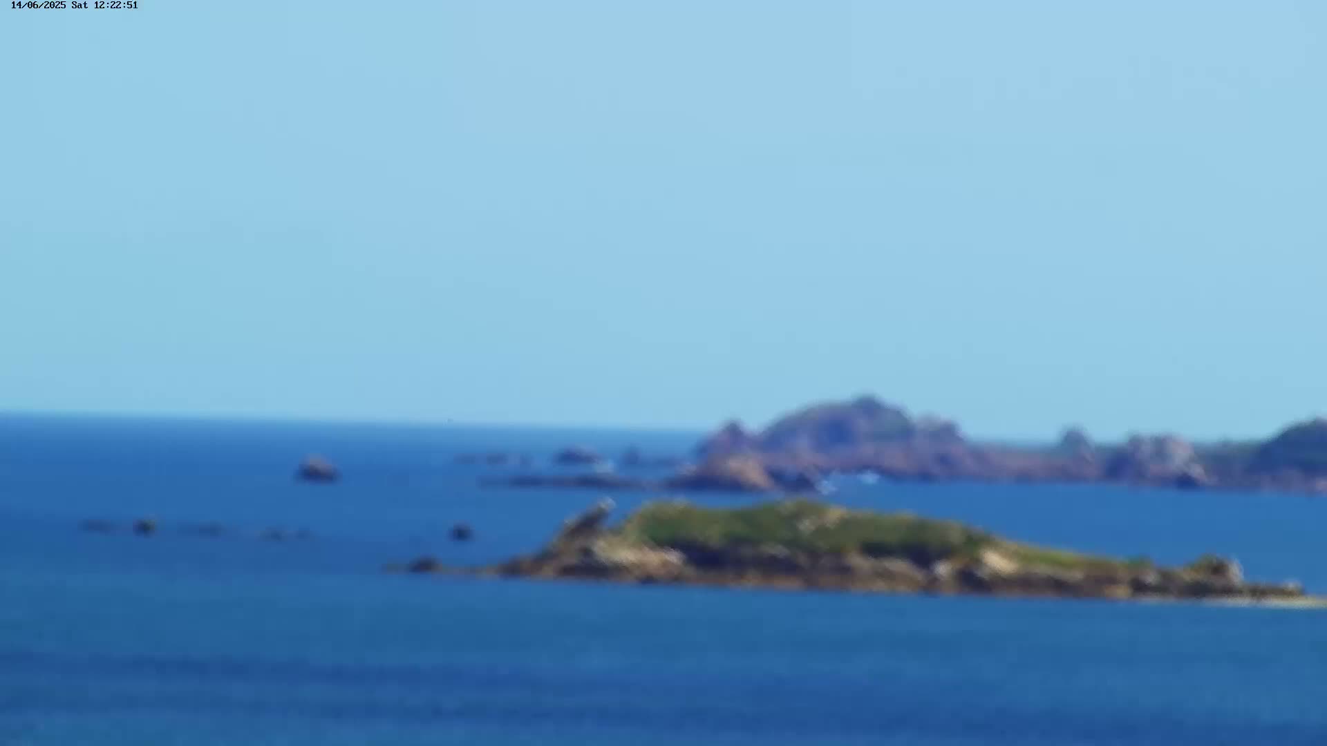 A distant view of several small, rocky islands in a calm, blue ocean under a clear sky.