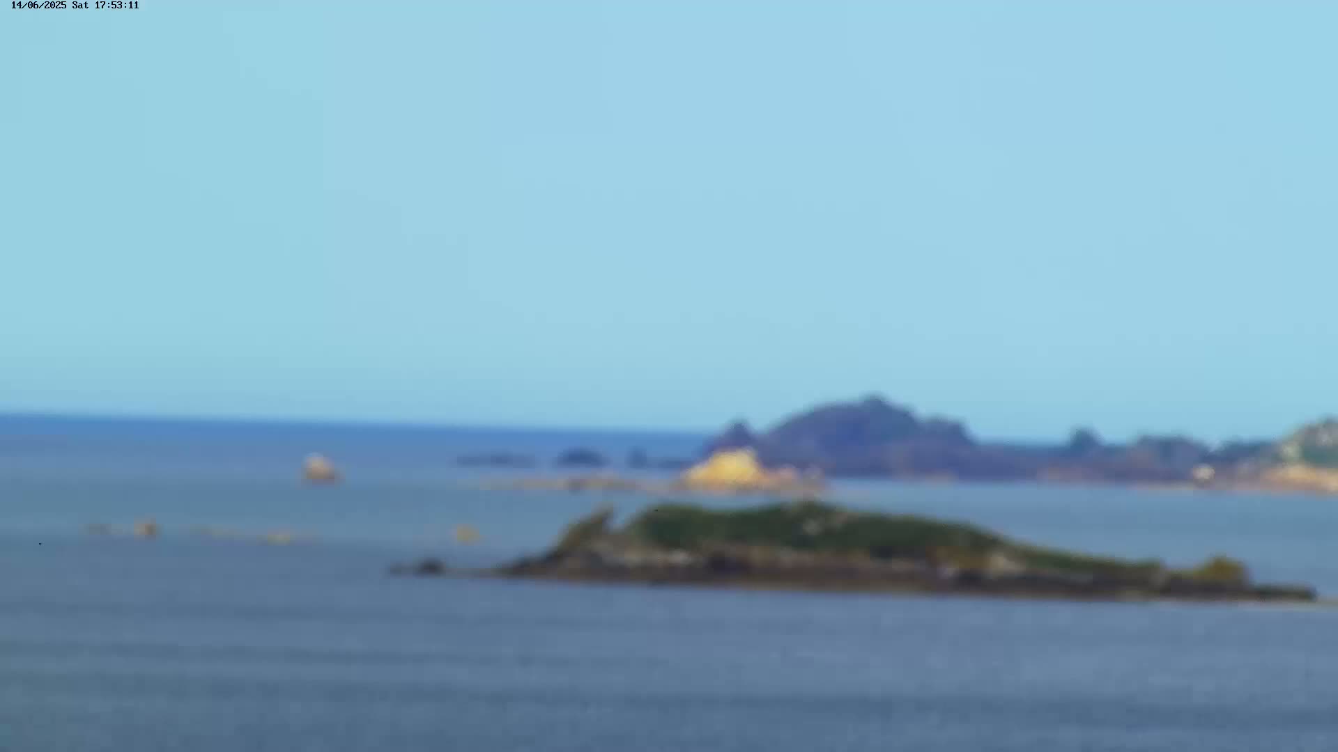 A blurry, distant view of a small, vegetated island in calm ocean water under a clear, light blue sky.