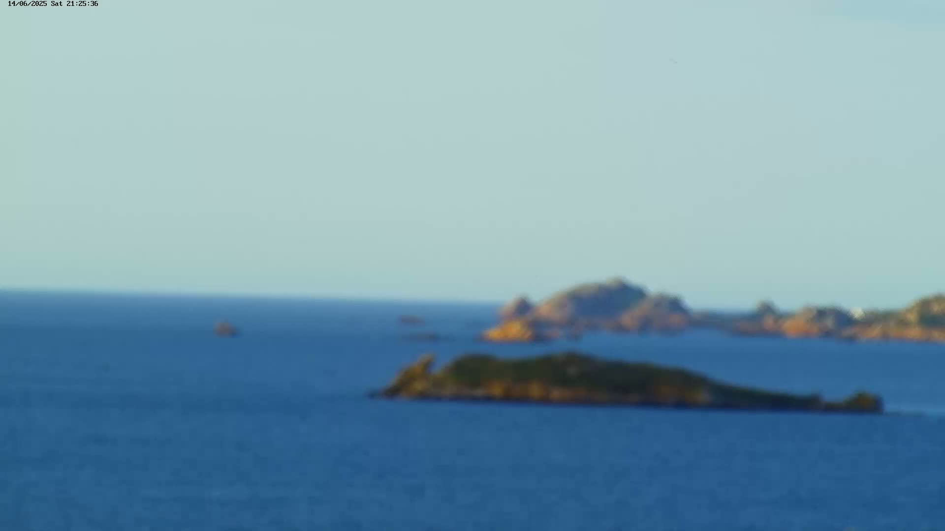 A blurry, distant view of a small, vegetated island in calm ocean water under a clear, light blue sky.