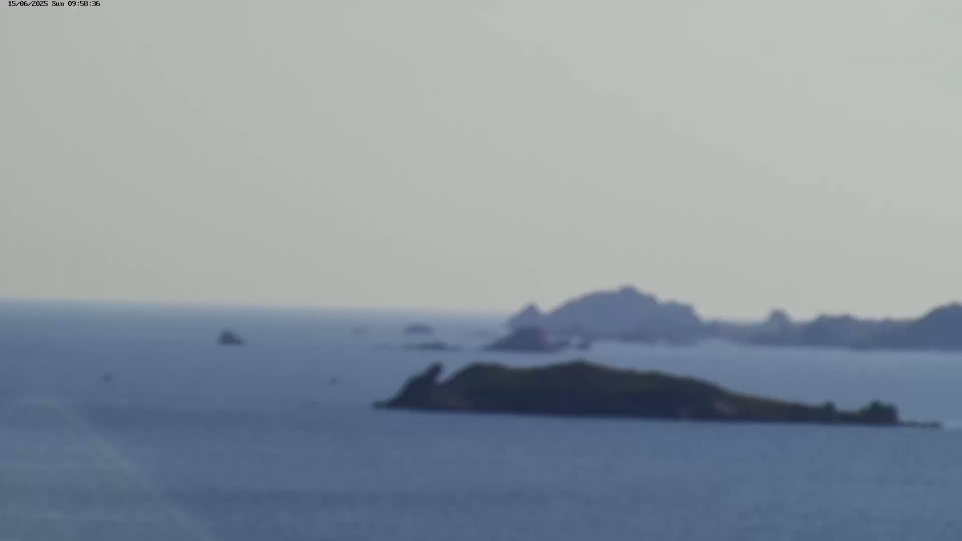 A hazy, overcast day shows a calm body of water with several small, dark islands in the middle and far distance.