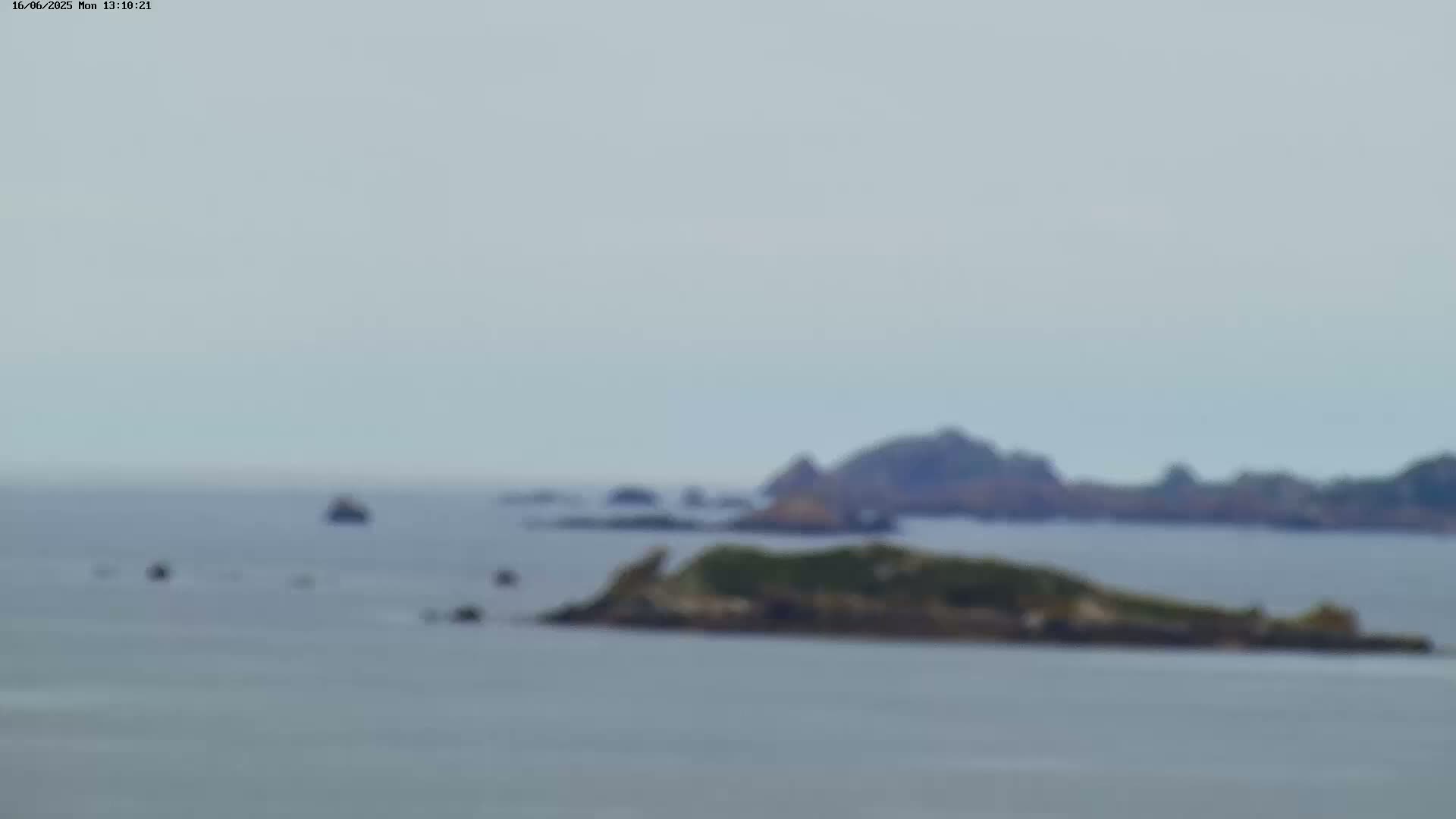 A blurry long shot shows a calm sea with several small islands and a few distant boats under an overcast sky.