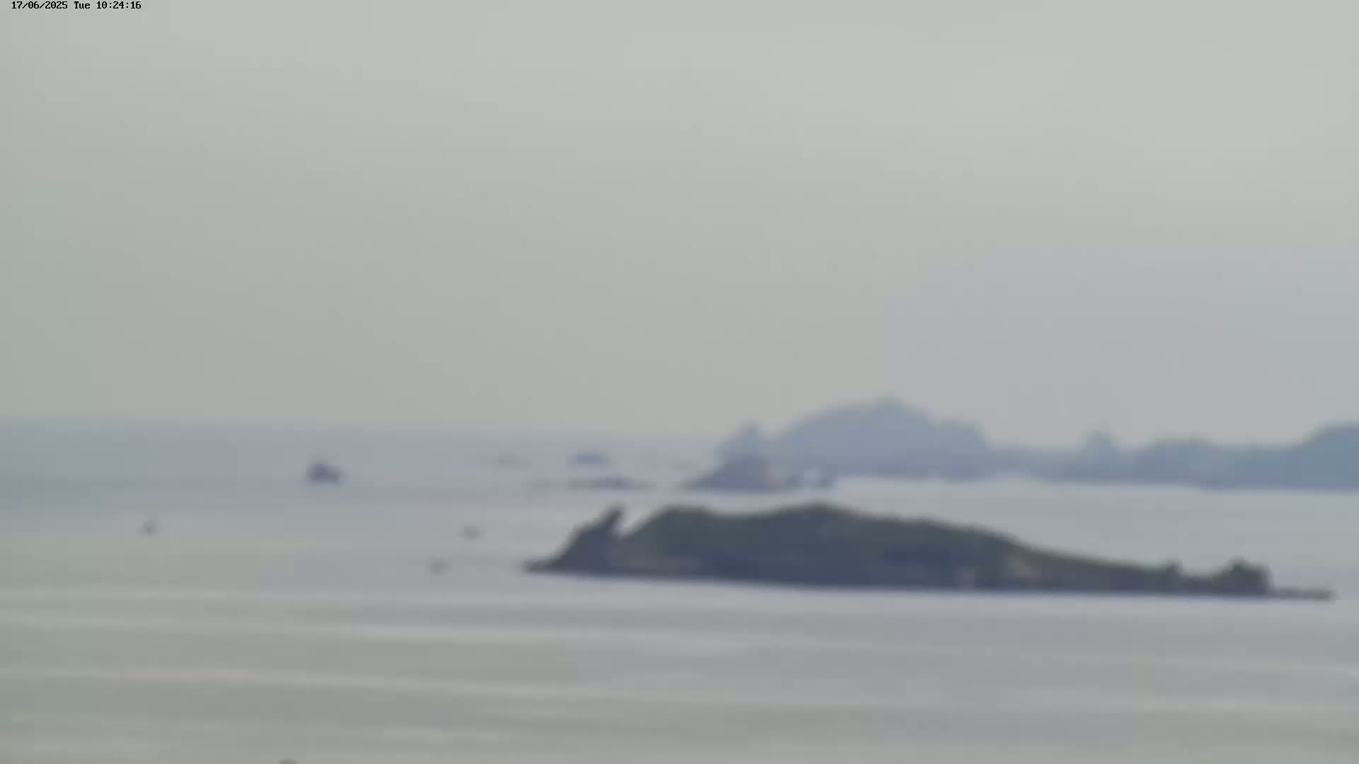 A hazy, overcast view shows a calm body of water with several small, dark islands in the mid-ground and a distant, indistinct shoreline.