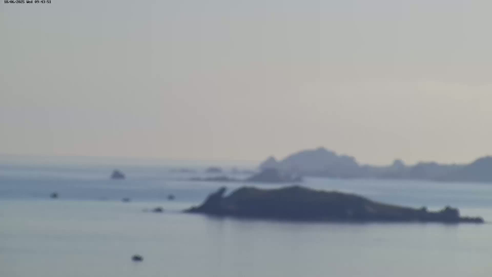 A hazy, calm ocean scene features several small, dark islands and a few distant, larger landmasses under a light-grey sky.