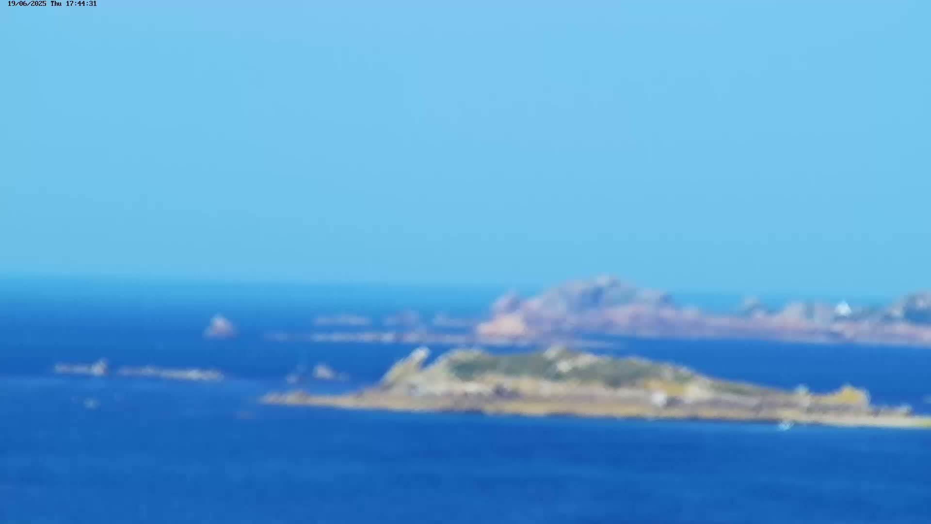 A blurry, distant view of rocky islands and blue ocean under a clear blue sky.