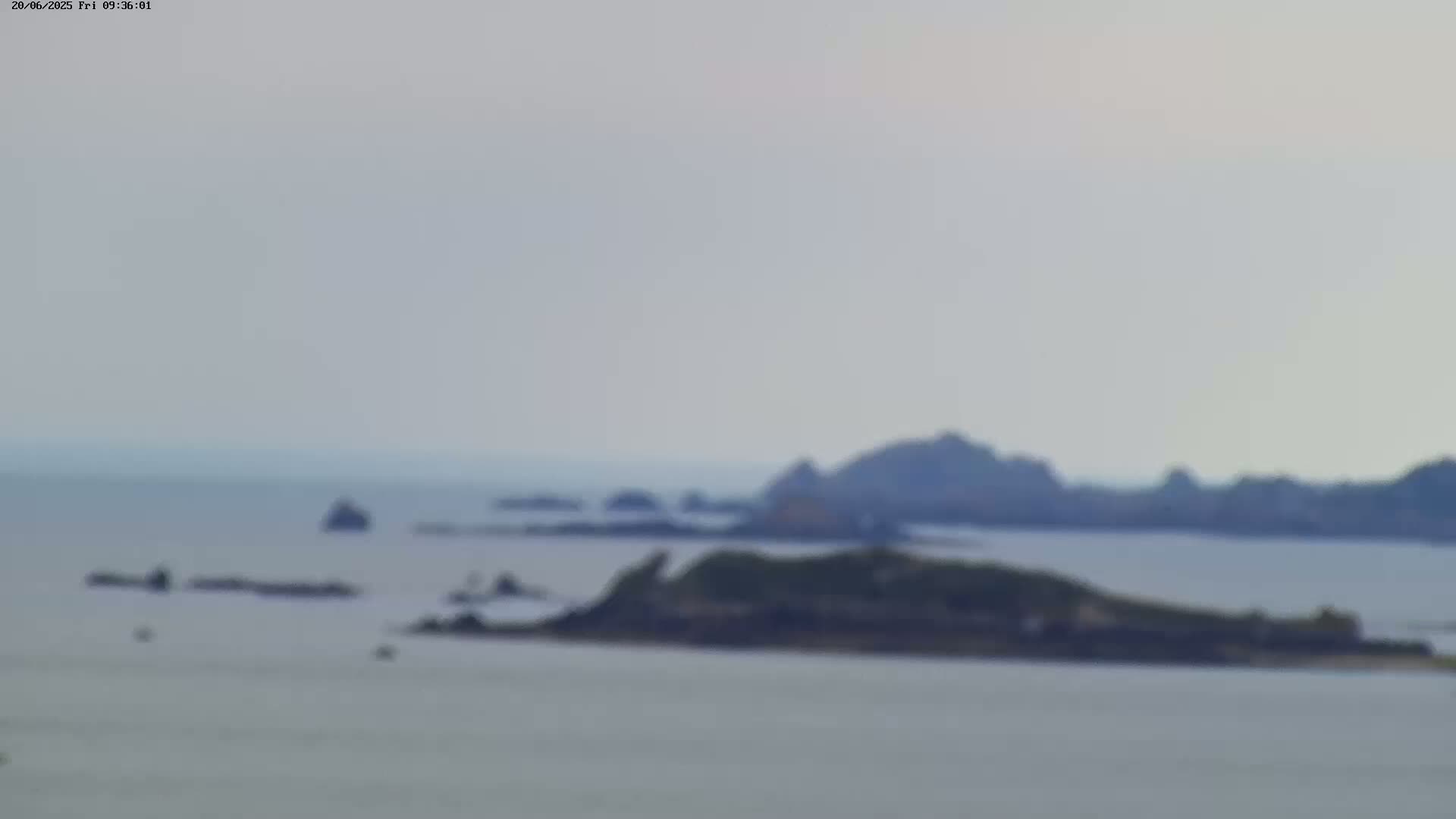 A blurry, distant view shows several small, dark islands in a calm, light-grey sea under an overcast sky.
