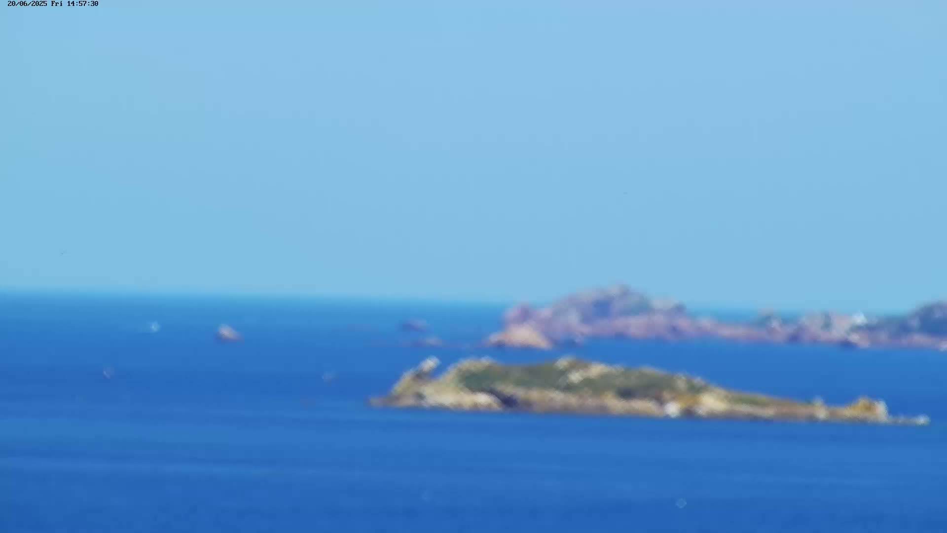 A hazy, sunny day shows a distant view of several small islands surrounded by calm blue ocean water.