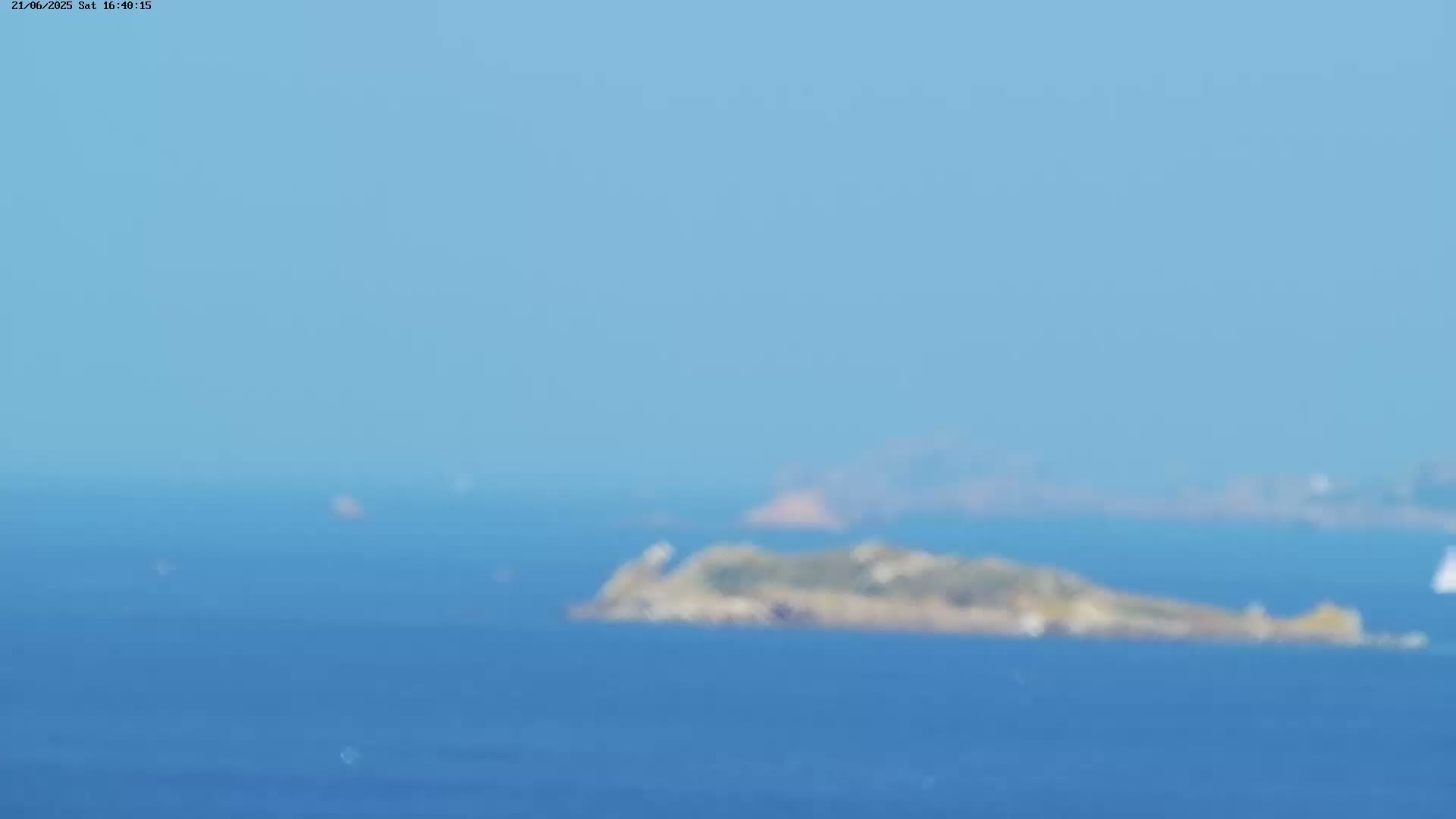 A hazy, clear day reveals a small, distant island in a calm, blue ocean.