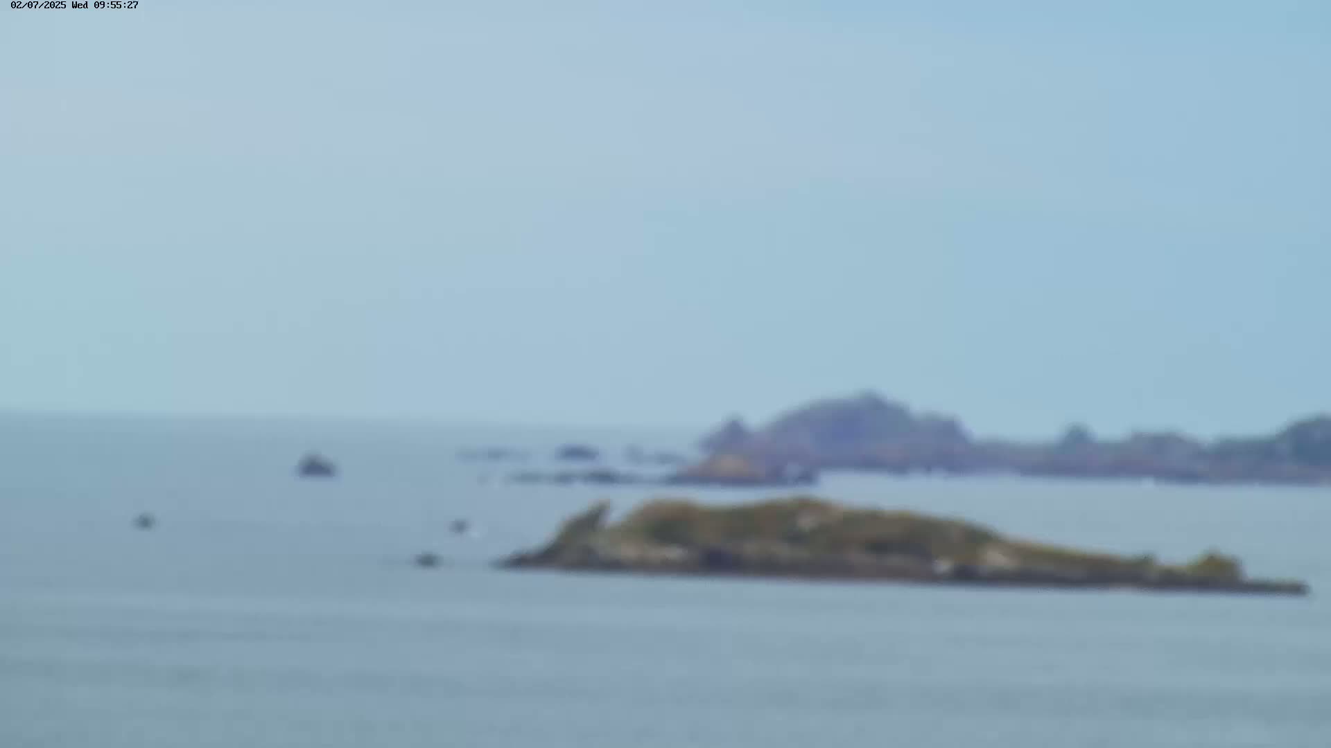 A blurry long shot shows a calm body of water with several small islands and a few distant boats under a hazy sky.