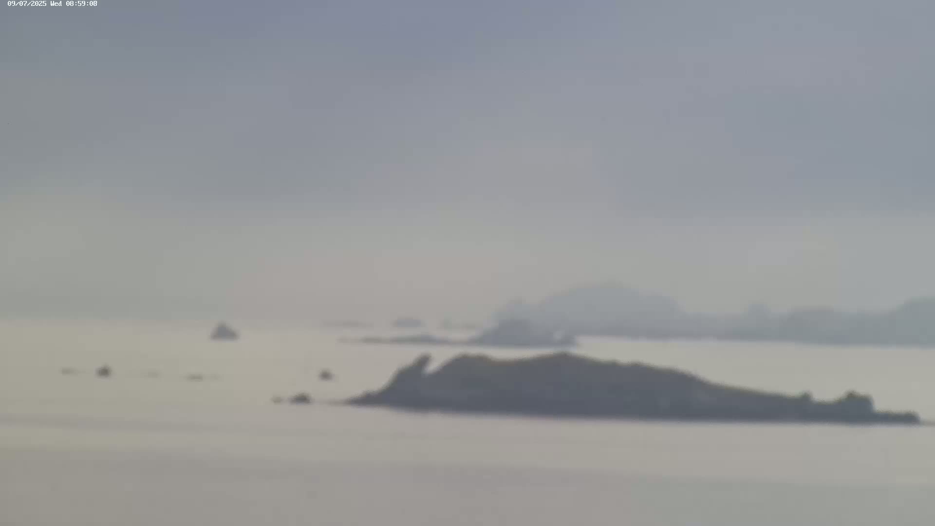 A hazy view shows several small, dark islands and outcroppings in a calm body of water.