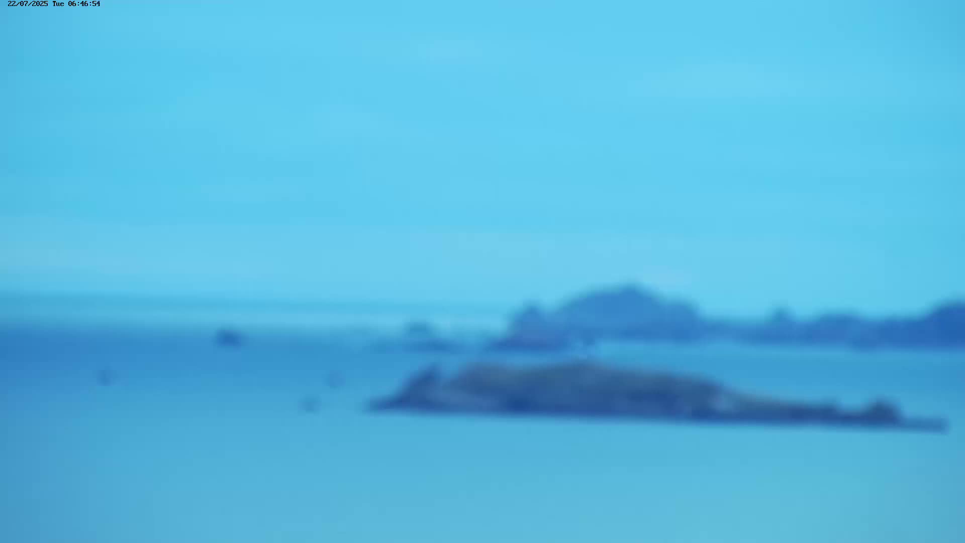 A blurry image shows a calm, light-blue ocean with dark-blue islands and a hazy sky.