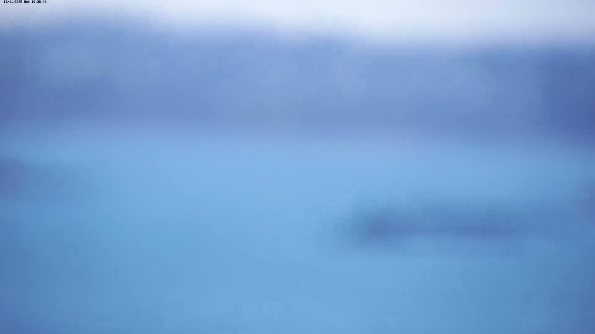A heavily blurred outdoor scene displays an overcast sky over a vast body of water, rendered in various shades of blue.