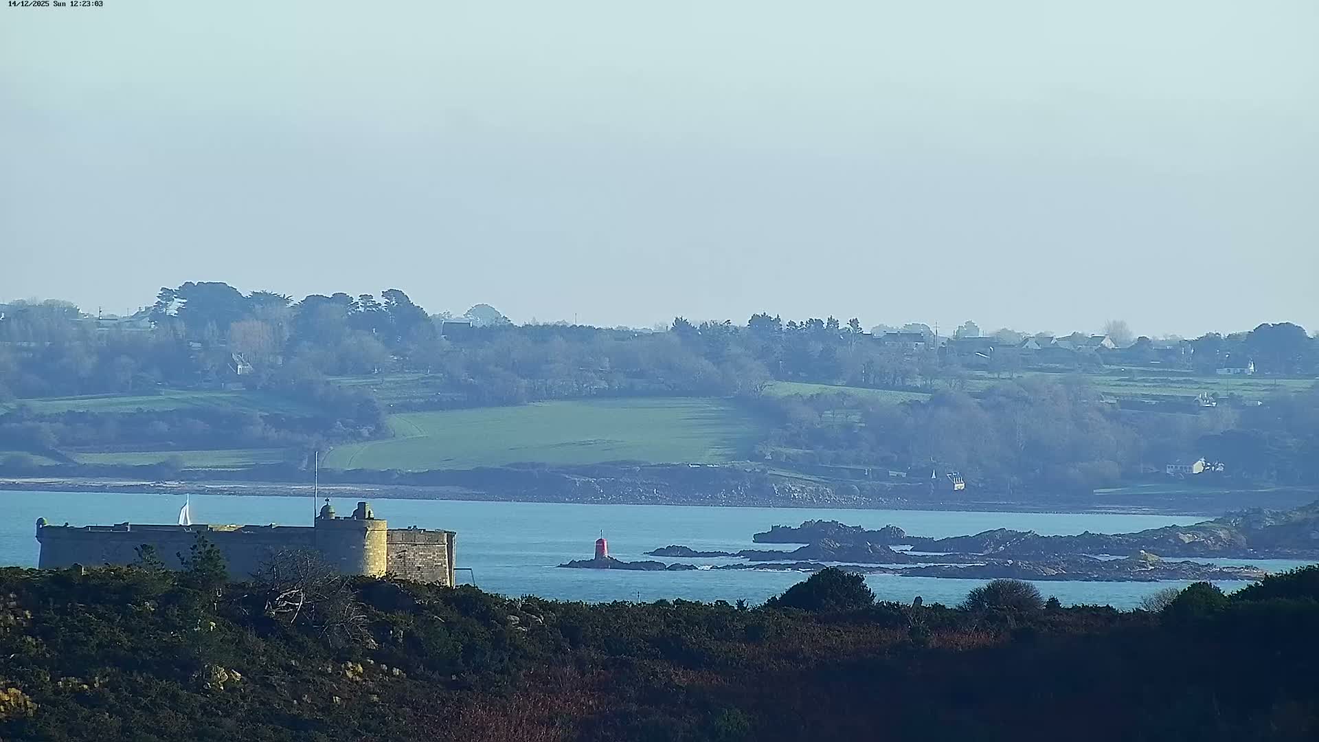 A heavily blurred outdoor scene depicts a light sky over dark, indistinct distant land, separated by calm blue water featuring a blurry dark horizontal shape in the middle, under hazy daytime conditions.