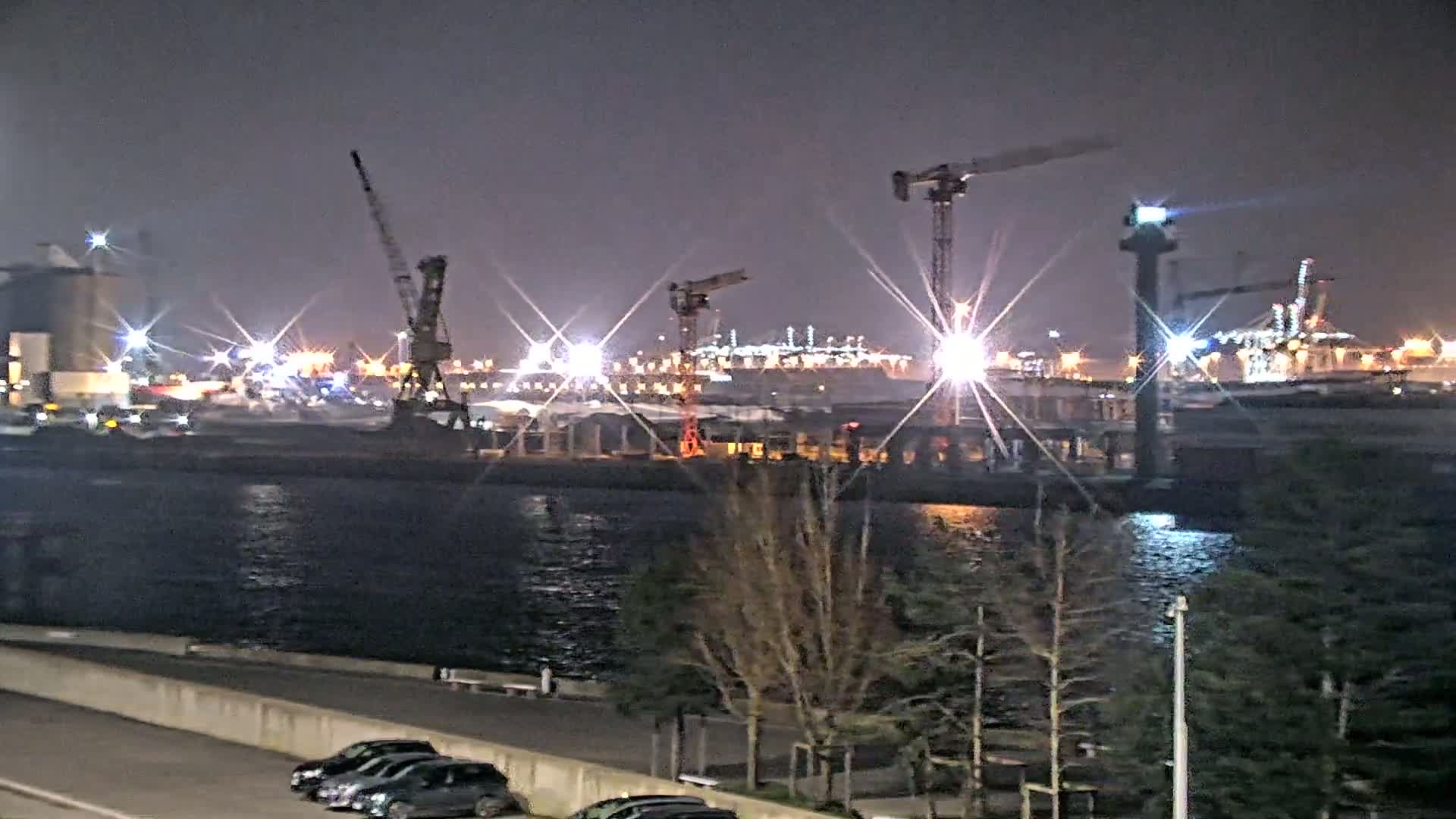 A nighttime view of a busy port with several cranes and bright lights reflecting on the water.