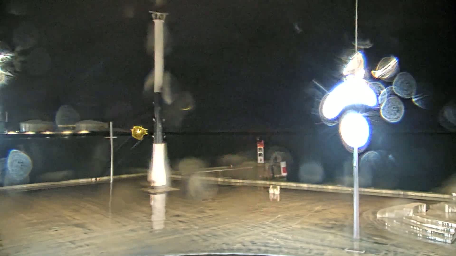 A nighttime, rain-slicked waterfront scene features a tall, slender light post and a smaller lighthouse in the distance.