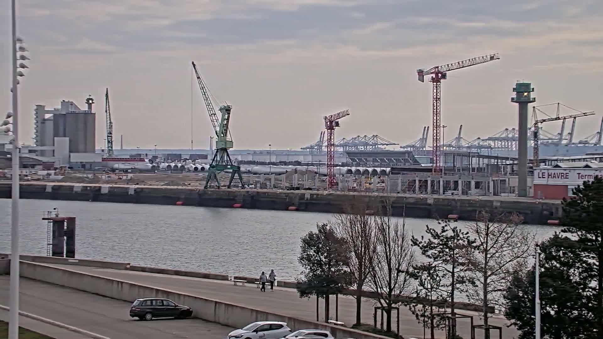 A view of a harbor with several cranes, industrial buildings, and construction under an overcast sky.