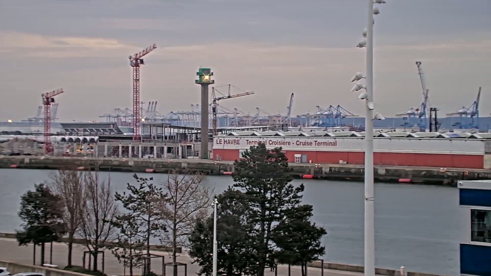 A harbor scene under an overcast sky shows a cruise terminal under construction, with several cranes and other port activity in the background.
