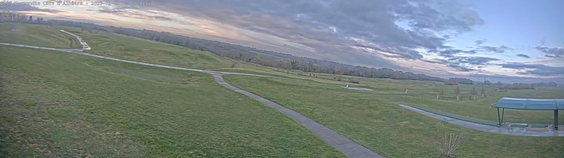 A sprawling green golf course with paved pathways under a partly cloudy sky.