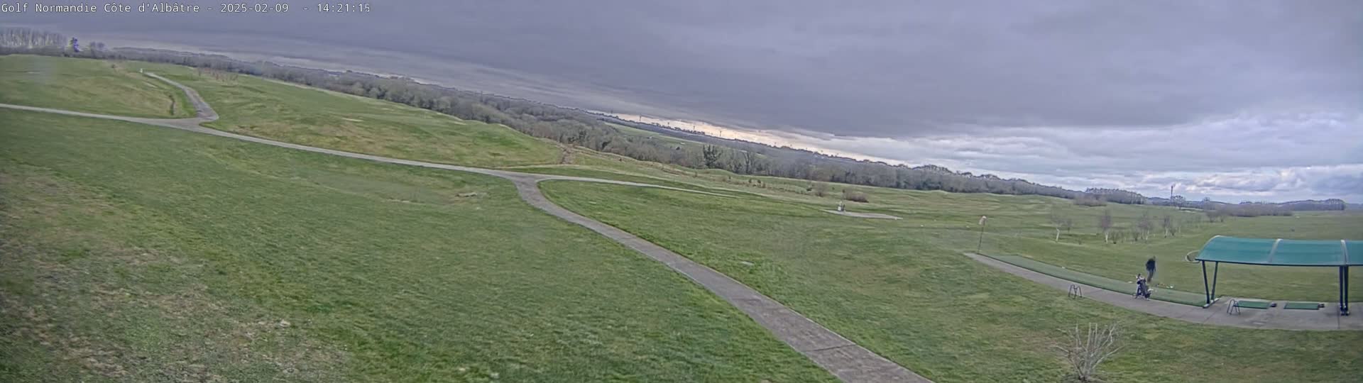 A golf course with a driving range, under a cloudy sky.