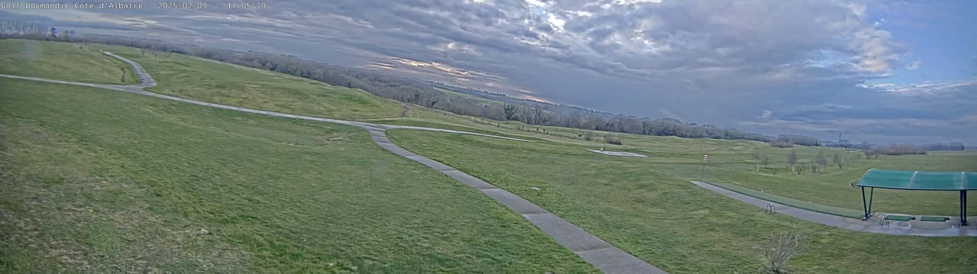 A paved path winds through a grassy golf course under a mostly cloudy sky.