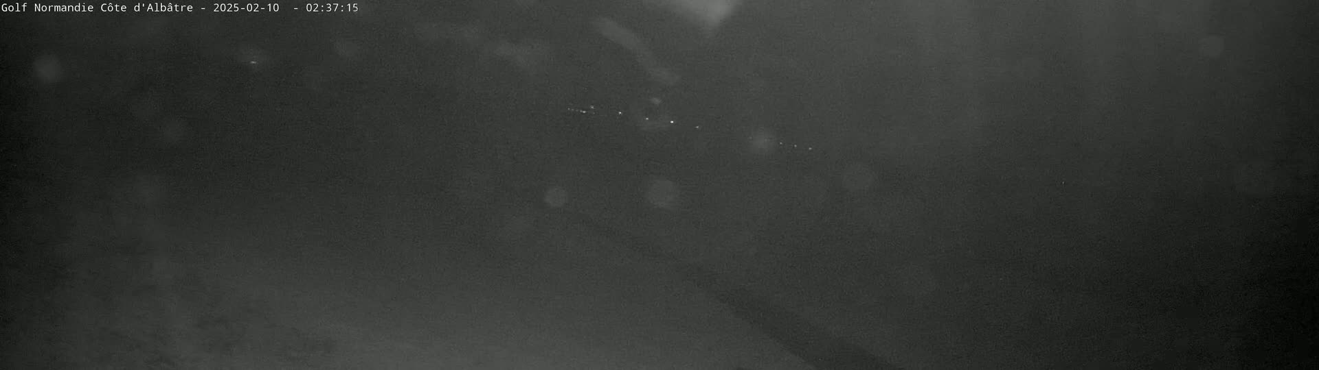 A blurry, dark nighttime image shows a few faint lights in the distance under a seemingly clear sky.