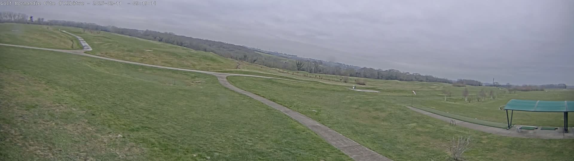 A view of a golf course on an overcast day shows a path winding through grassy fairways toward a covered driving range.