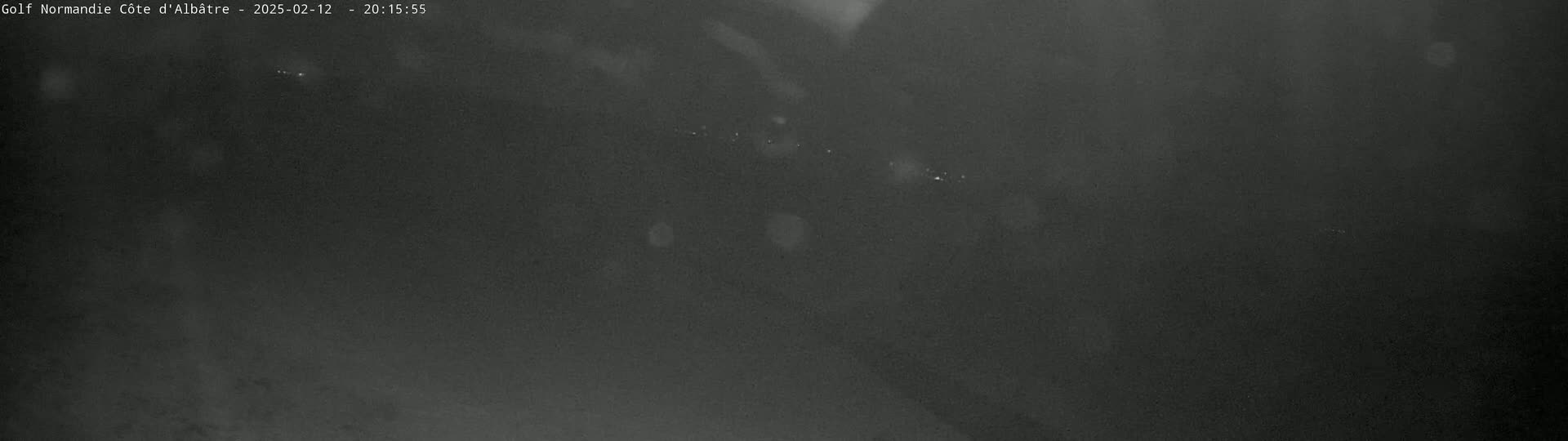 A dark, nighttime image shows a few distant lights in the hazy darkness.