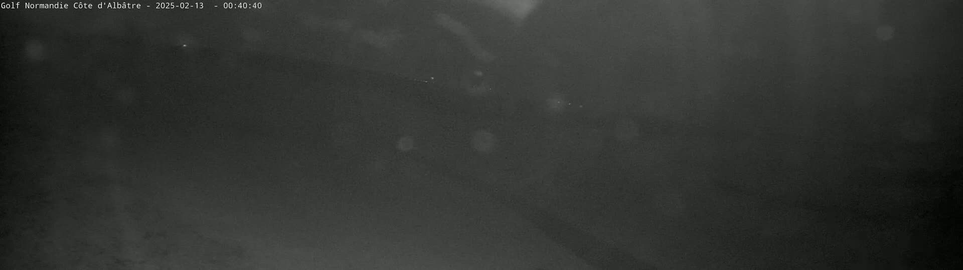 A dark, blurry nighttime image shows a few faint lights in the distance under an overcast sky.