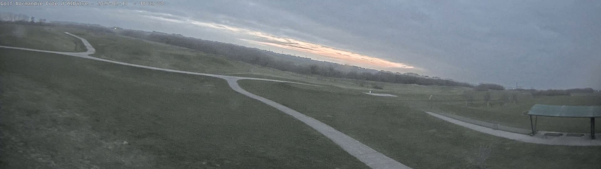 A paved path curves through a grassy field under a cloudy sky with a hint of pink at the horizon.