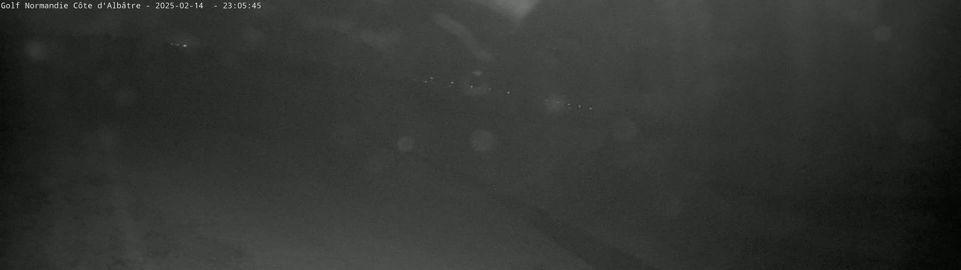 A dark, blurry nighttime image shows a few faint lights in the distance under a cloudy sky.