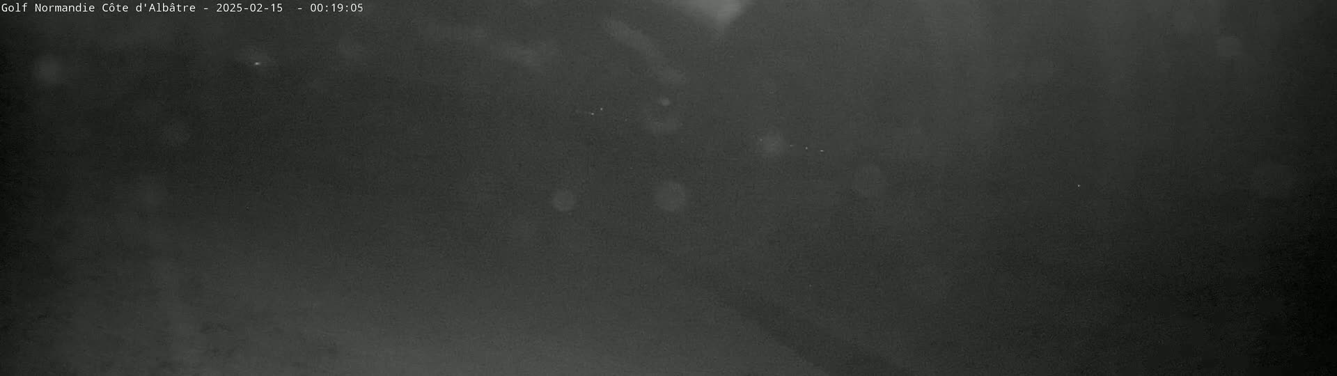 A nighttime, dark gray image shows a blurry, indistinct view of an outdoor scene under a cloudy sky.