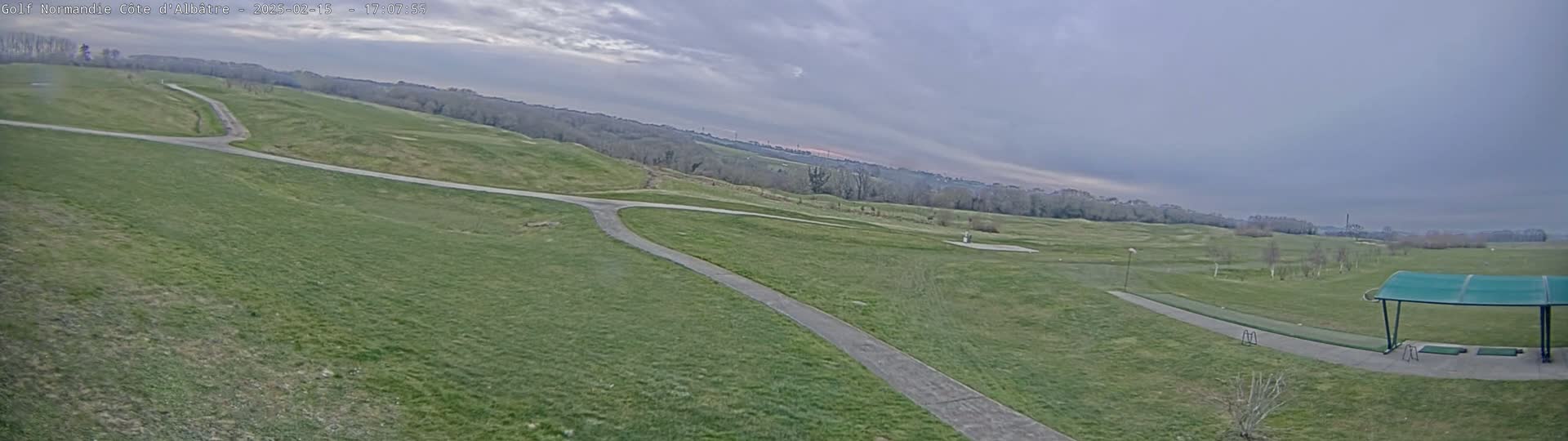 A wide, grassy golf course with paved paths under an overcast sky.