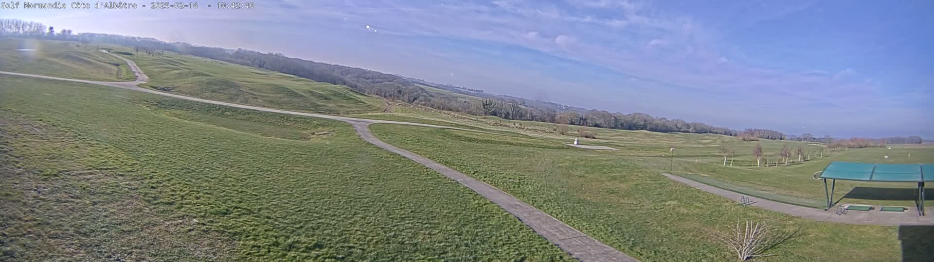 A sprawling green golf course under a mostly sunny sky stretches across a gently rolling landscape.