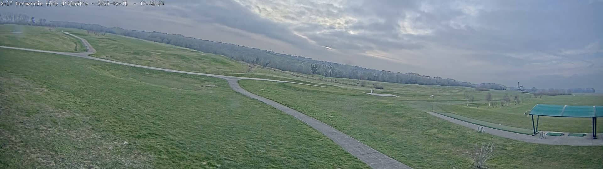 A sprawling, grassy golf course with paved pathways under an overcast sky.