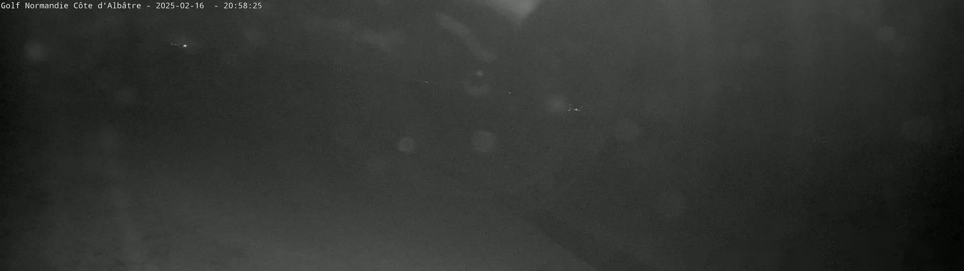 A dark, nighttime image shows a mostly black scene with a few faint, distant lights.