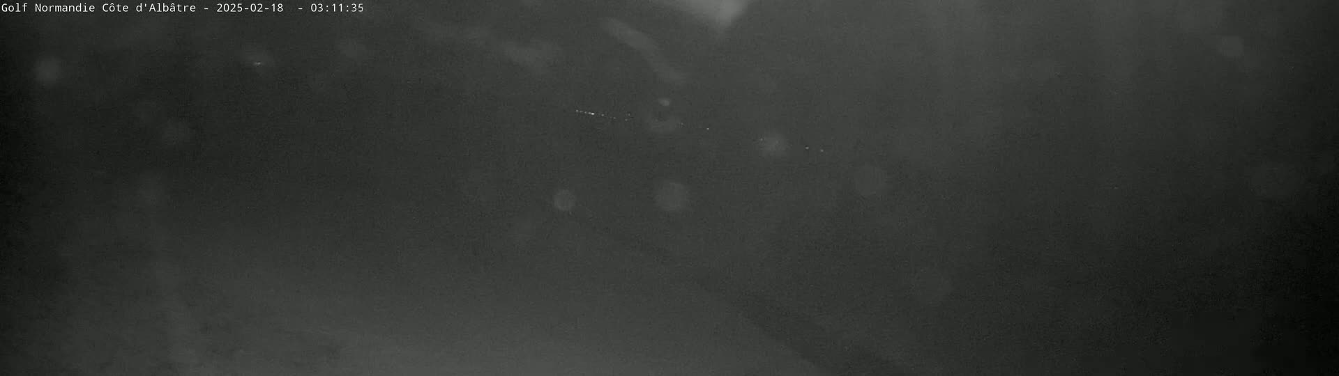 A dark, blurry image shows a nighttime outdoor scene with light precipitation or mist.