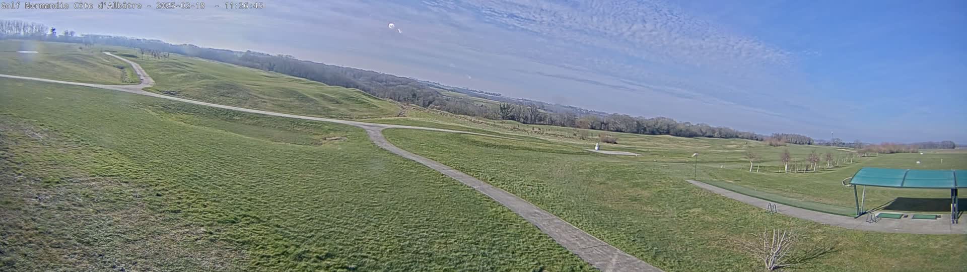 A sprawling green golf course with paved pathways stretches under a mostly clear, sunny sky.