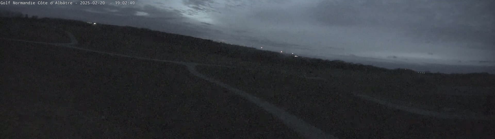 A dark, overcast sky looms over a hilly, mostly dark landscape at dusk.